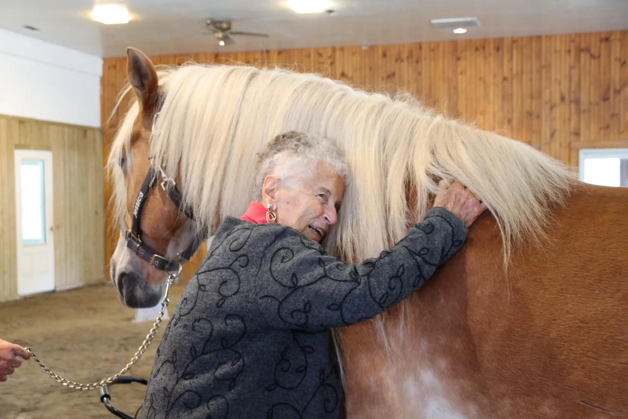 Atria resident, Marilyn, smiles as she hugs Jessica the therapy pony