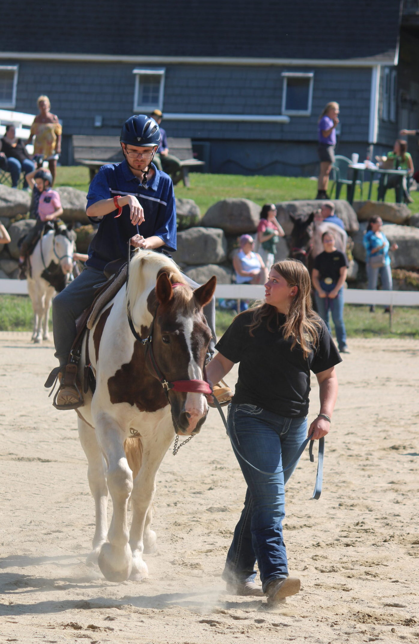 Matthew riding a large brown and white horse during our annual horse show. A young woman is leading his horse and looking back at him.