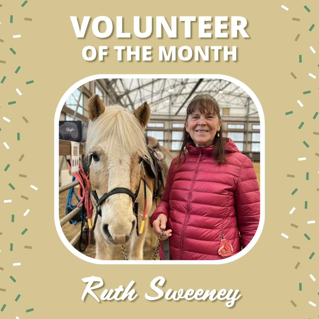 A woman smiles while standing next to a blonde horse