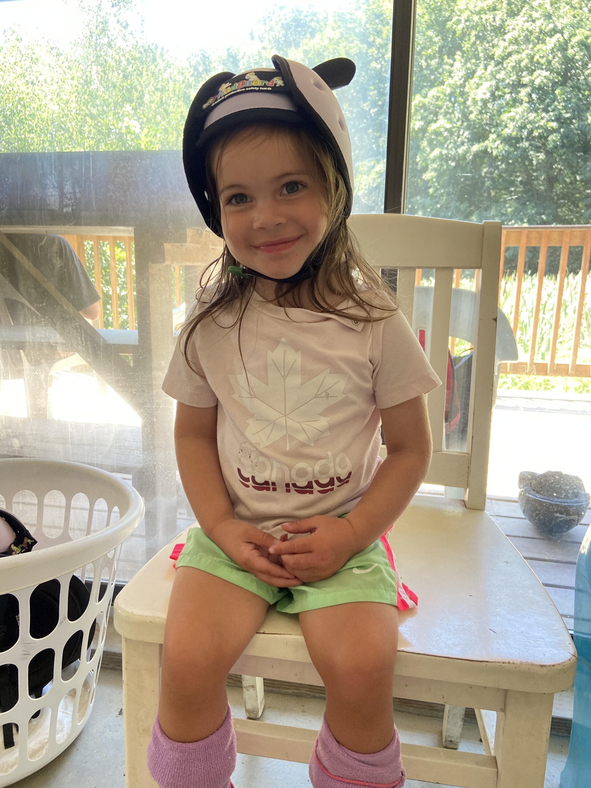 March rider of the month, Remy, sits on a chair smiling with helmet on before her lesson. She is about 4 years old.