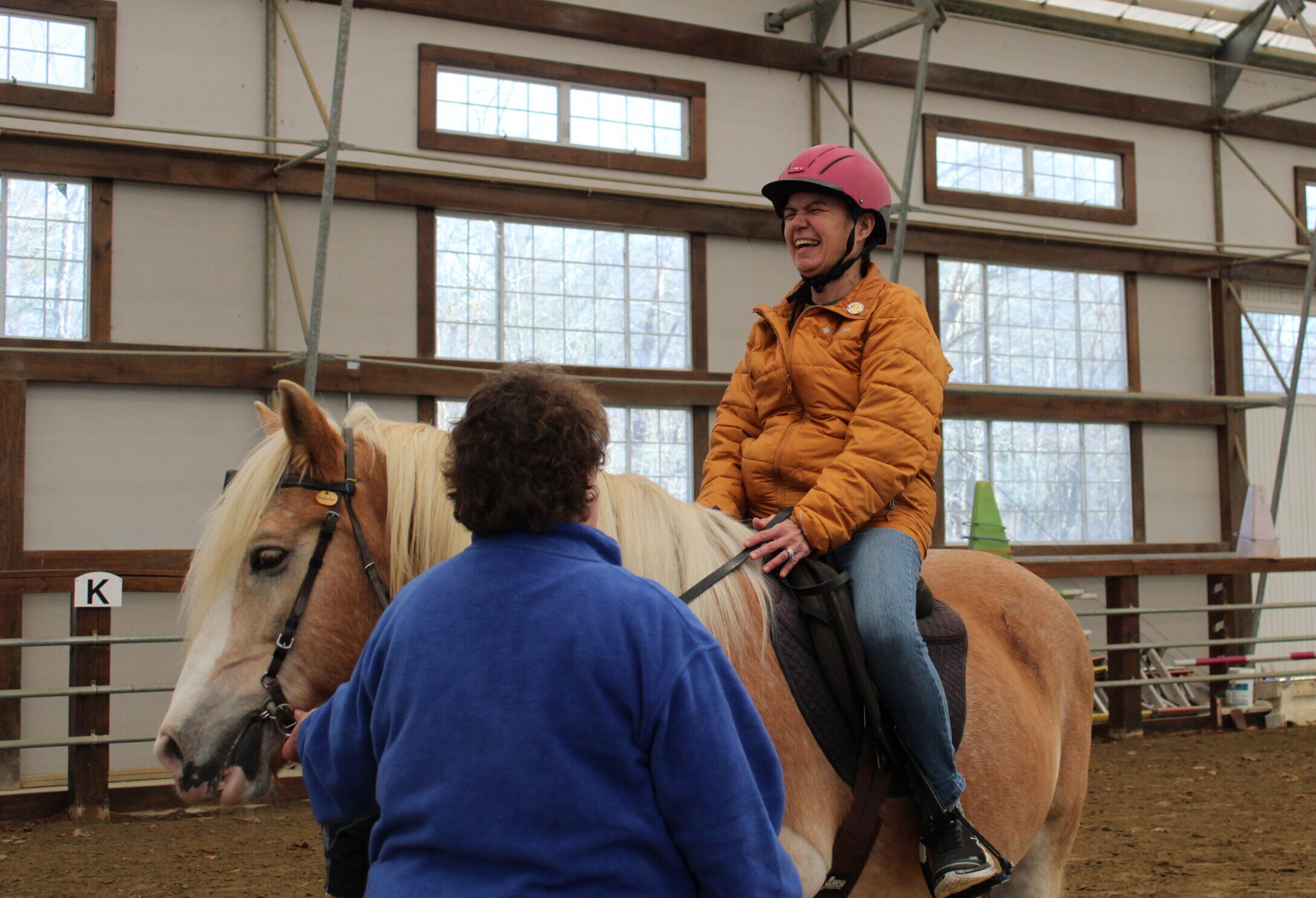 A woman laughs while riding a blonde horse